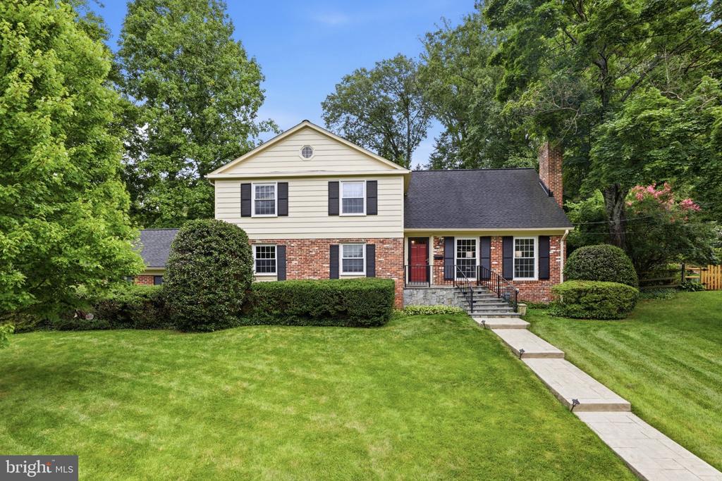 Two-story cream-and-brick home with a red front door, broad lawn, and walkway.