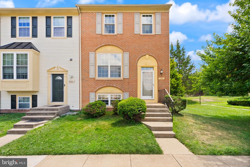 Brick-front townhouse with cream siding, front steps, shrubs, and a lawn.