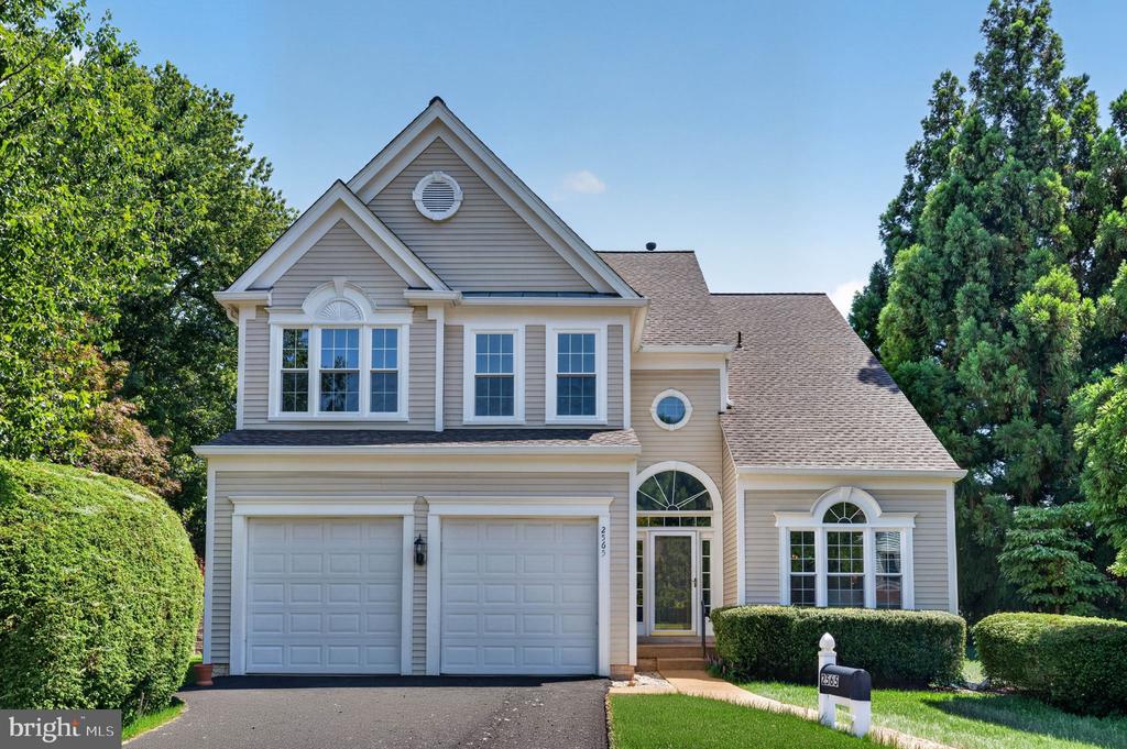 Two-story beige house with a two-car garage, arched entry, and green lawn.