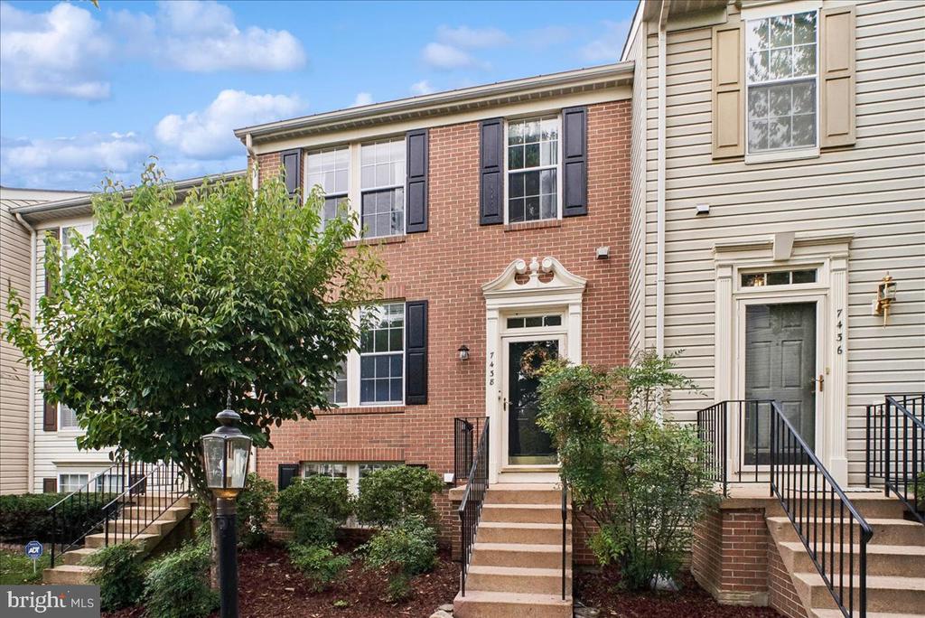 Red-brick townhouse with black shutters, a decorative entry, front steps, and landscaped shrubs.