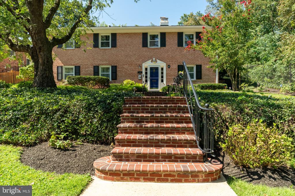 Two-story brick house framed by mature trees, with a wide brick staircase leading to the entrance.
