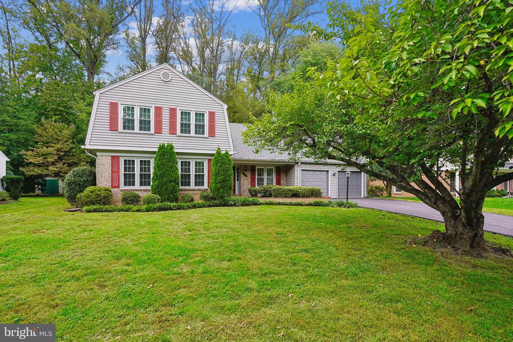 Two-story gray home with red shutters, brick facade, attached garage, and a broad green lawn.