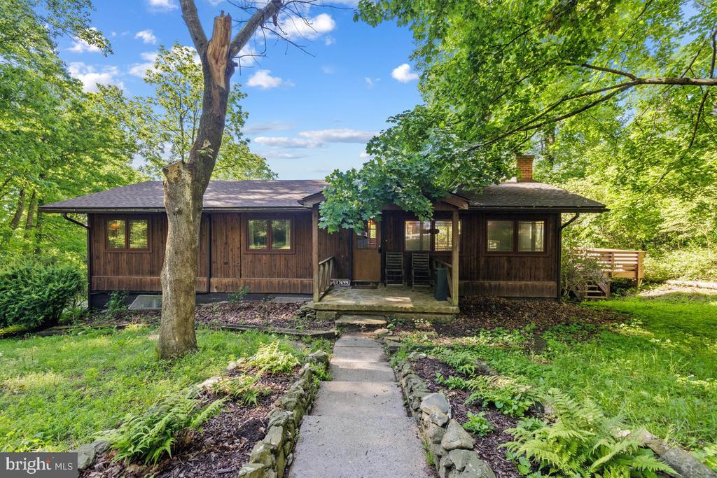 Wood-sided home framed by mature trees, with a covered porch and stone-edged walkway.