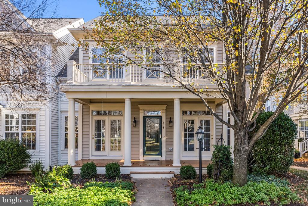 Two-story house with a covered porch, upper balcony, and mature autumn trees.