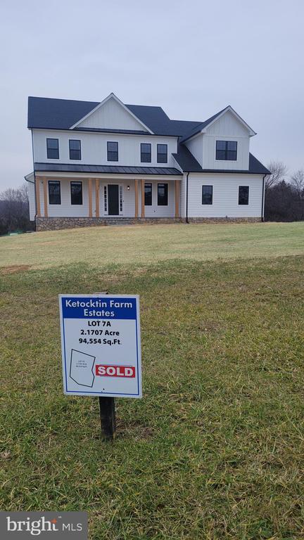 White two-story farmhouse on a grassy lot, with a SOLD sign in the foreground.