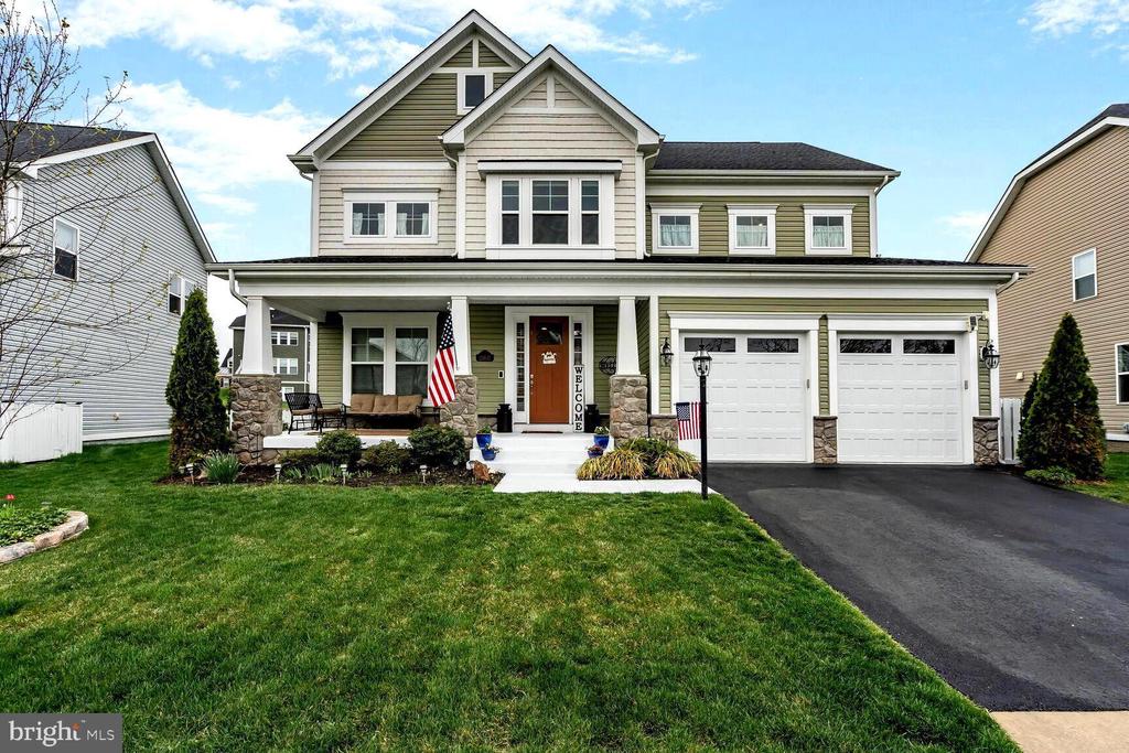 Two-story olive-sided home with a covered porch, stone columns, and a two-car garage.