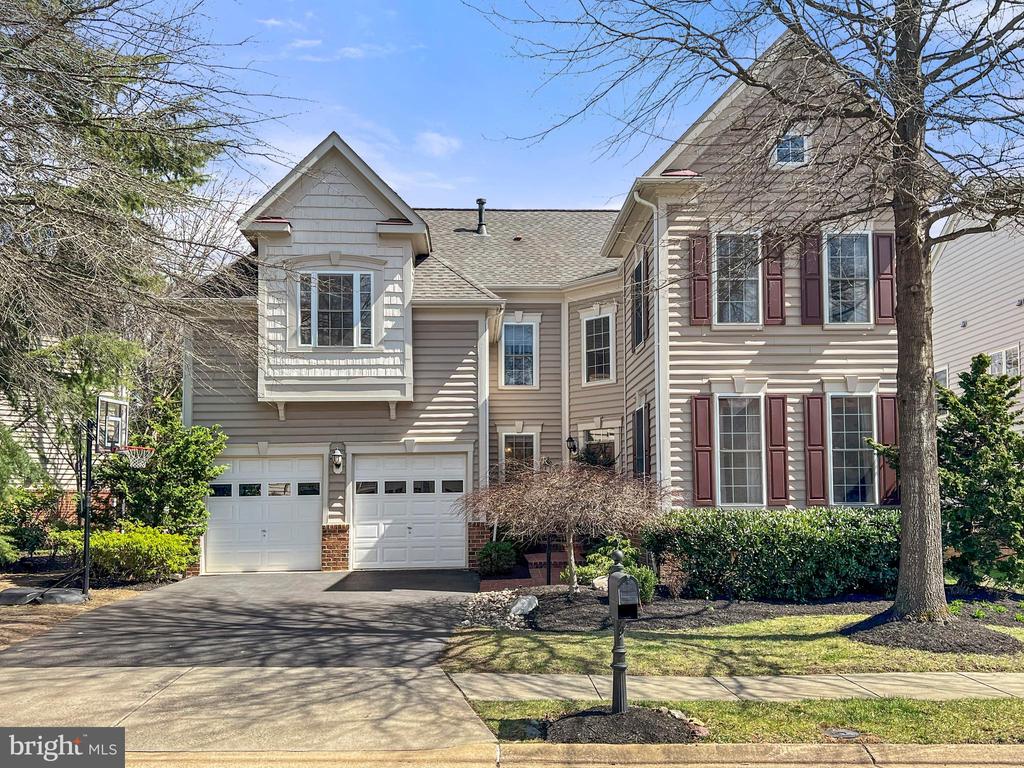 Two-story beige house with burgundy shutters, two garage doors, and a wide driveway.