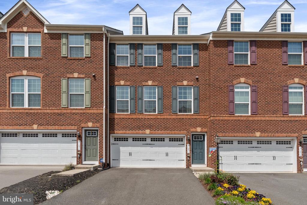 Attached brick townhouses with white garage doors, colorful shutters, and flower beds.