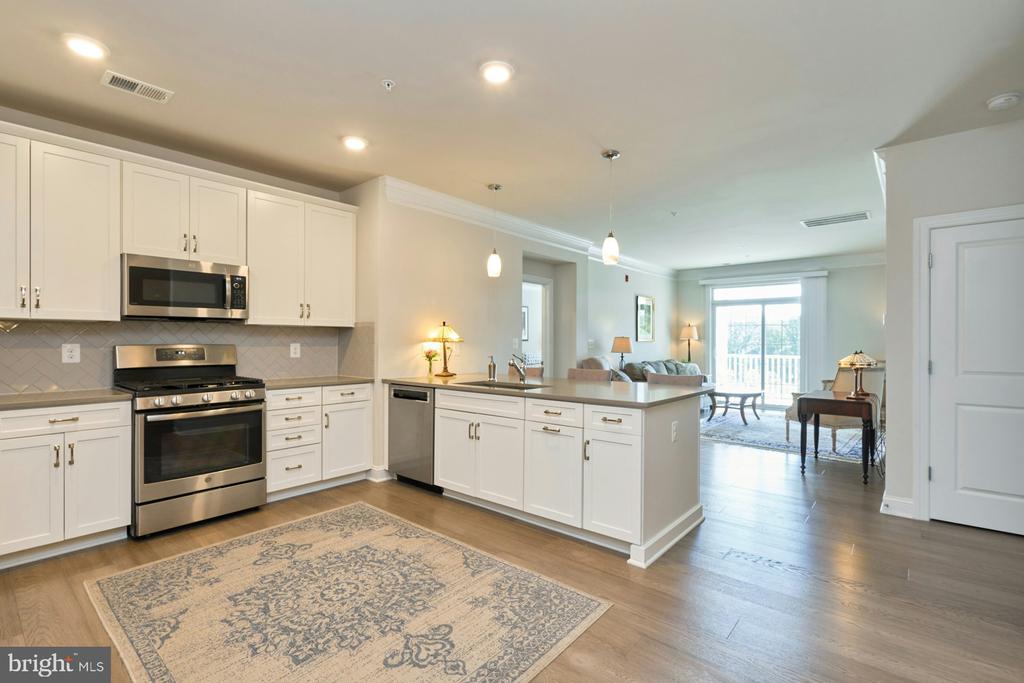 Open-plan kitchen with white cabinets, stainless steel appliances, and an island beside a bright living area.