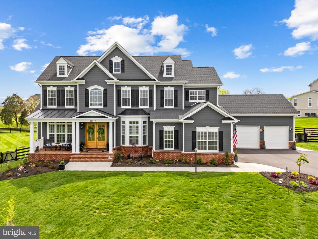 Two-story gray house with a covered porch, brick foundation, and attached three-car garage.