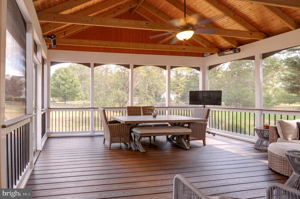 Screened porch with a vaulted wood ceiling, wicker seating, and views of the grassy yard and trees.