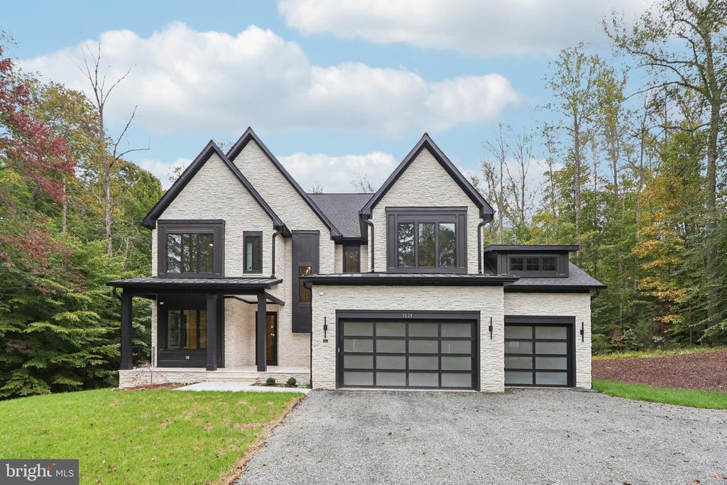 Modern two-story stone house with dark trim, two garage doors, and a wooded autumn setting.