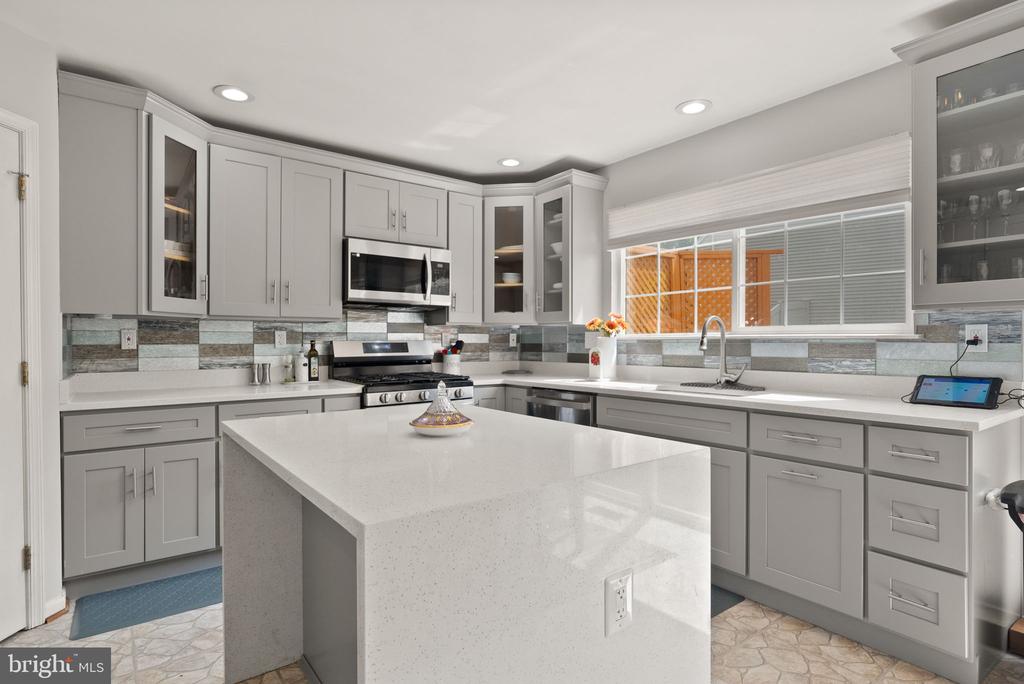 Renovated kitchen with gray cabinets, a large white island, and a multicolored tile backsplash.