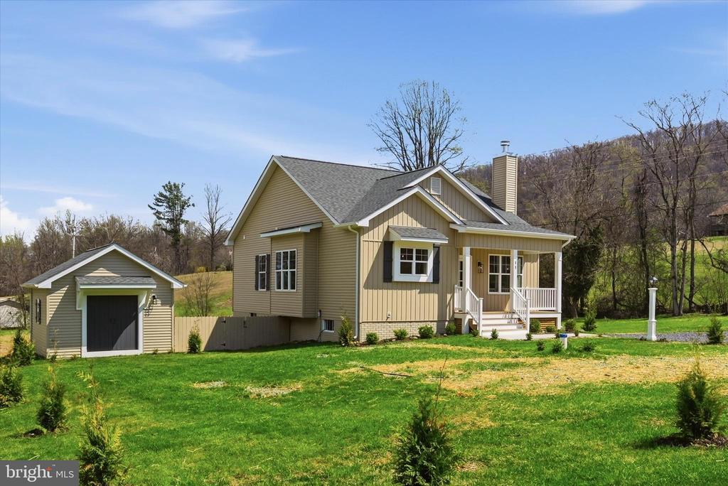 Beige house with a covered porch and detached garage on a green lawn.