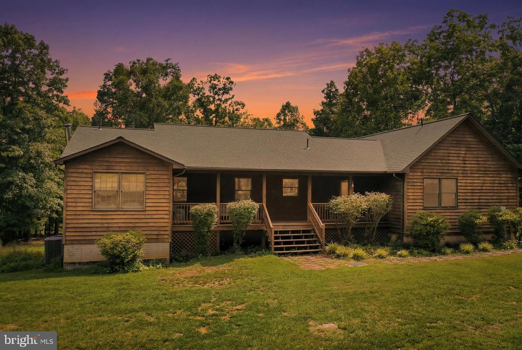 Wood-sided single-story home with a covered front porch, lawn, and mature trees at sunset.