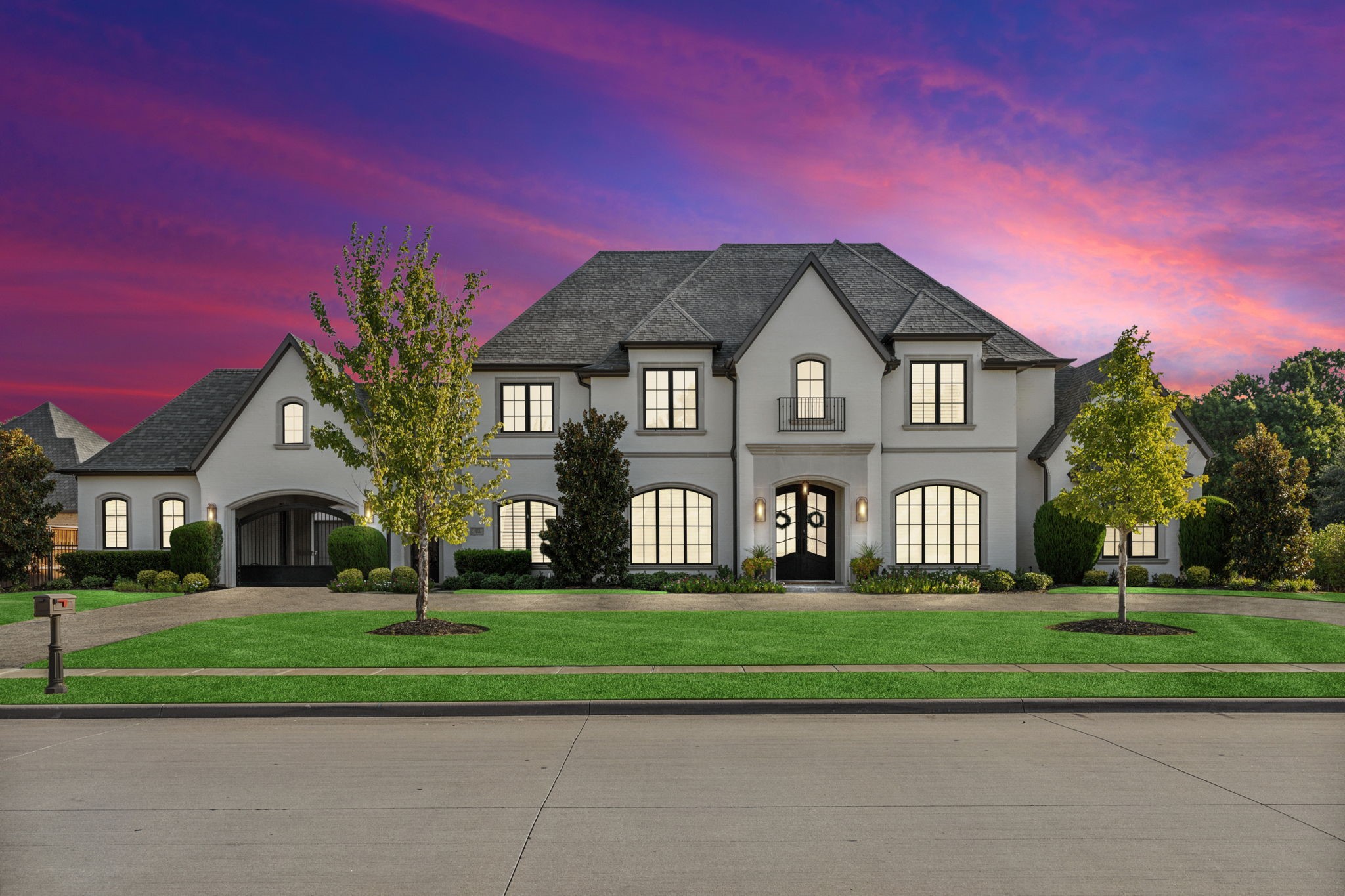 Large white two-story home with illuminated windows and landscaped lawn beneath a vivid dusk sky.