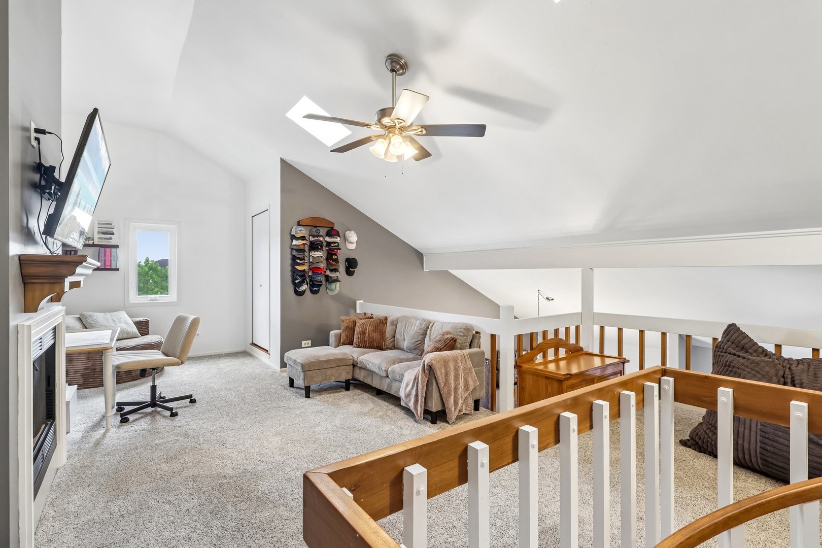 Furnished loft living area with vaulted ceiling, sectional sofa, fireplace, and wood-and-white railing.