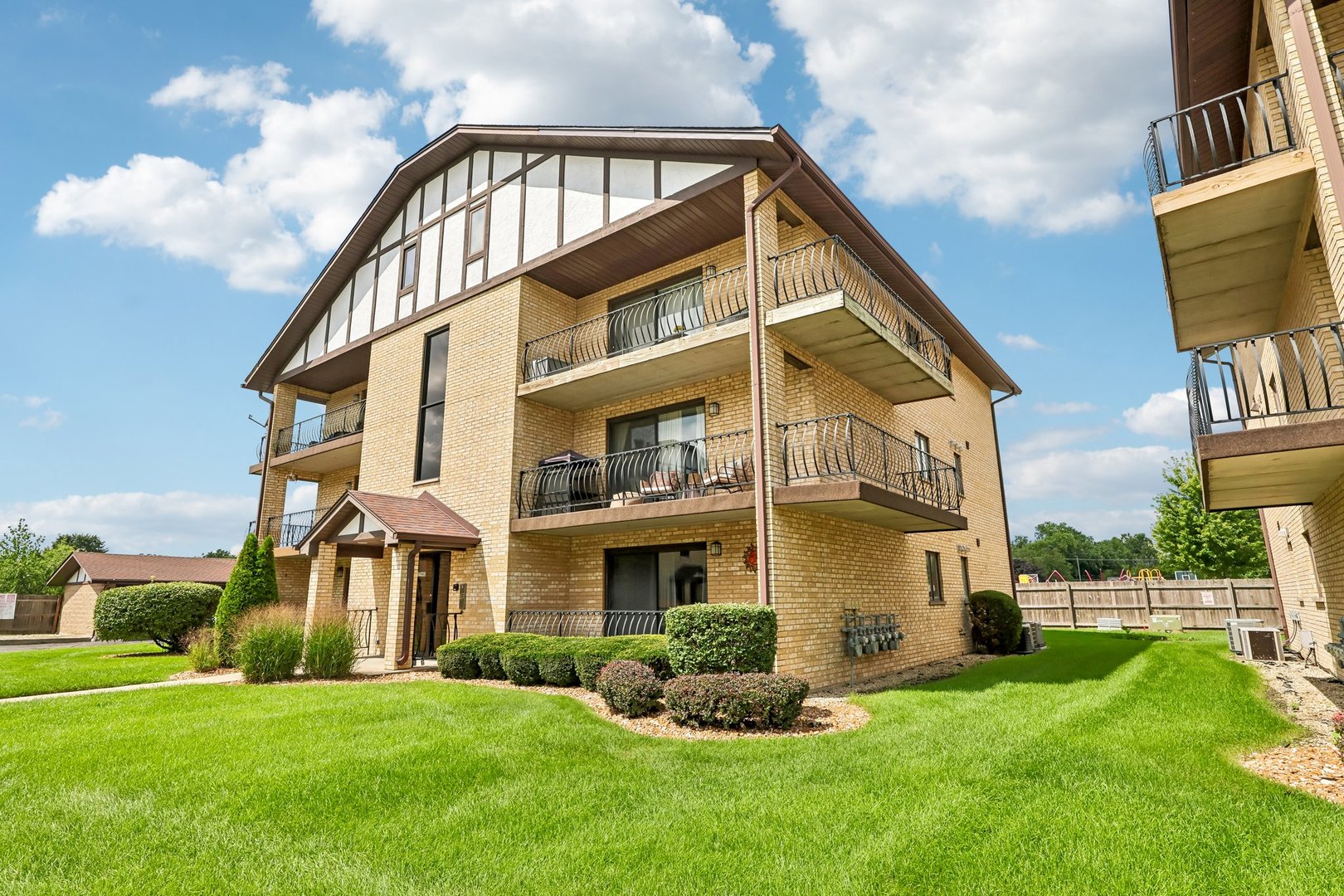 Yellow brick apartment building with multiple balconies and a landscaped lawn.