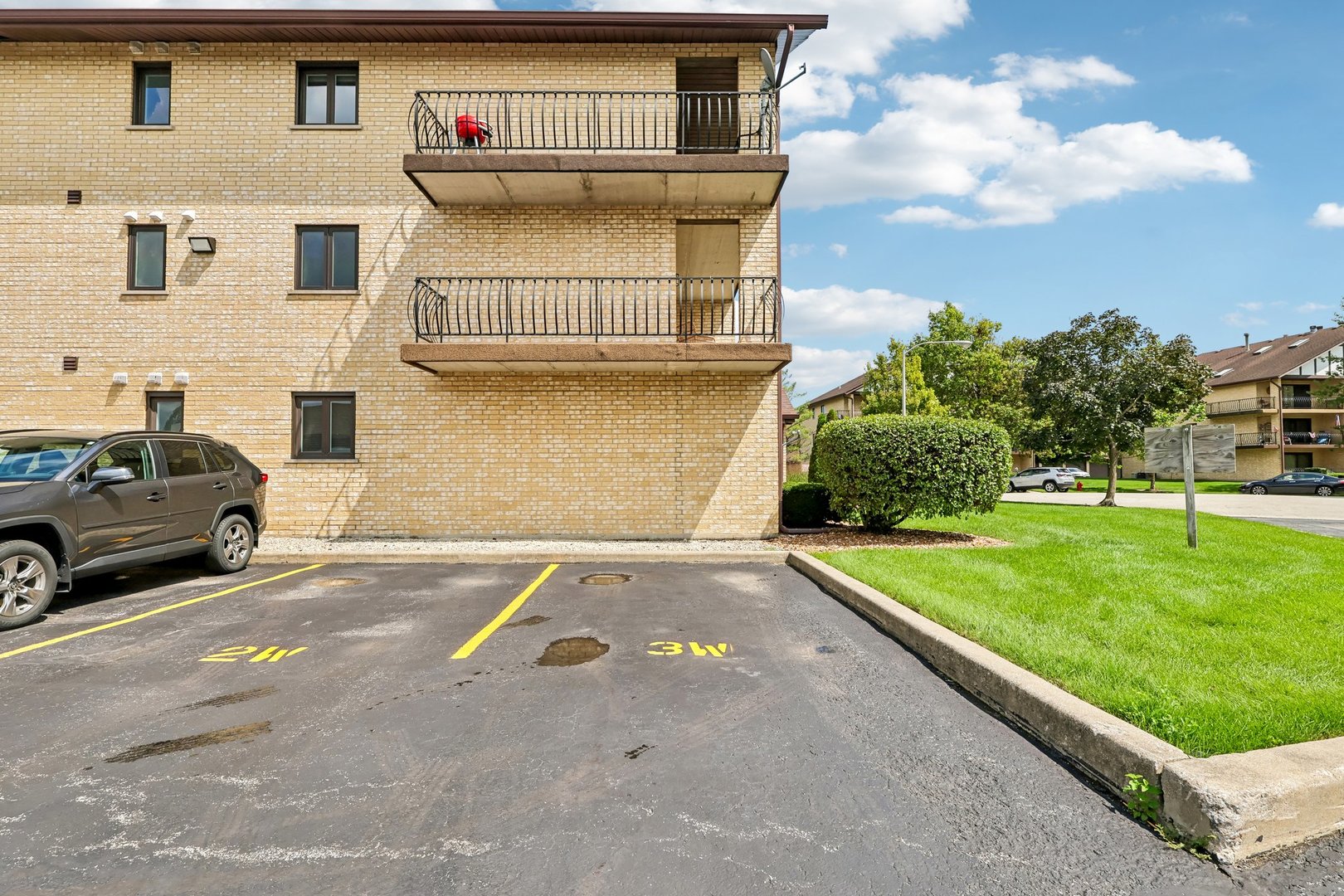 Tan brick apartment building with two balconies beside parking spaces marked 2W and 3W.