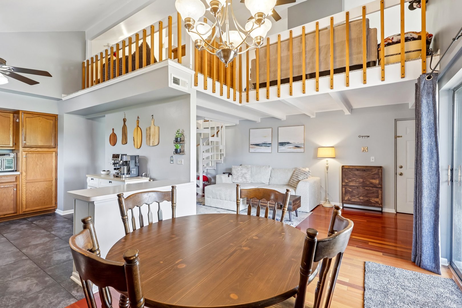 Open-plan dining and living area with a wooden table and loft overlooking the room.