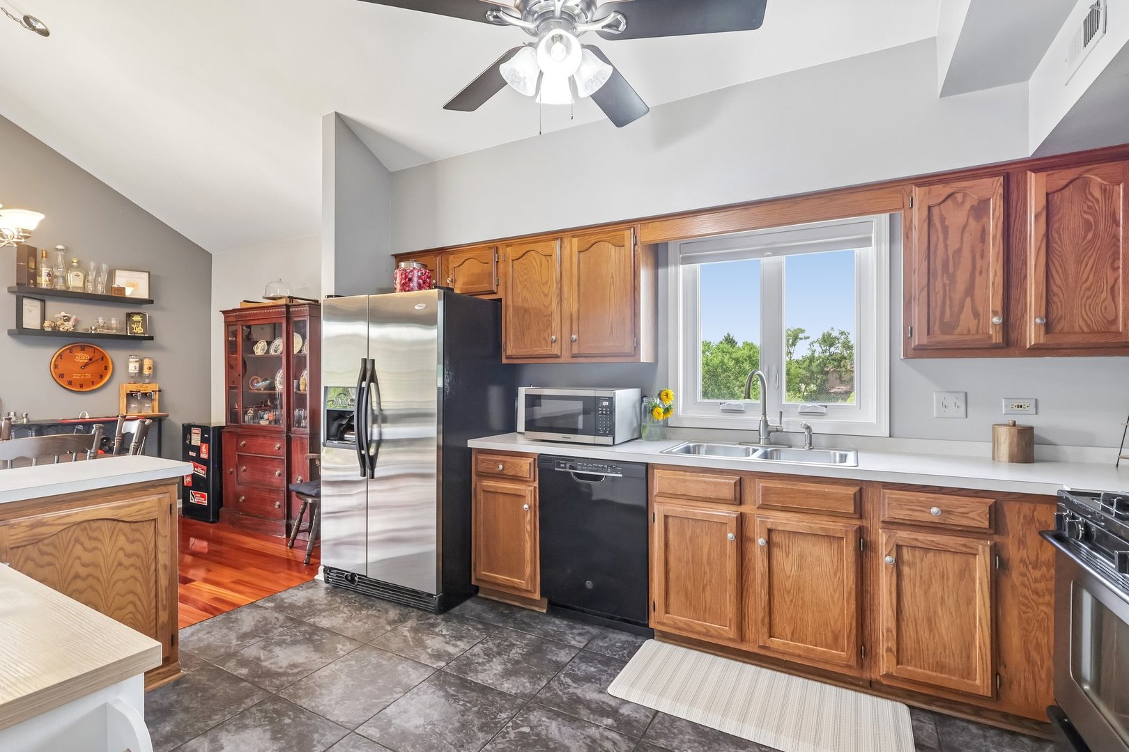 Kitchen with honey-colored wood cabinets, stainless steel refrigerator, and double sink beneath a window.