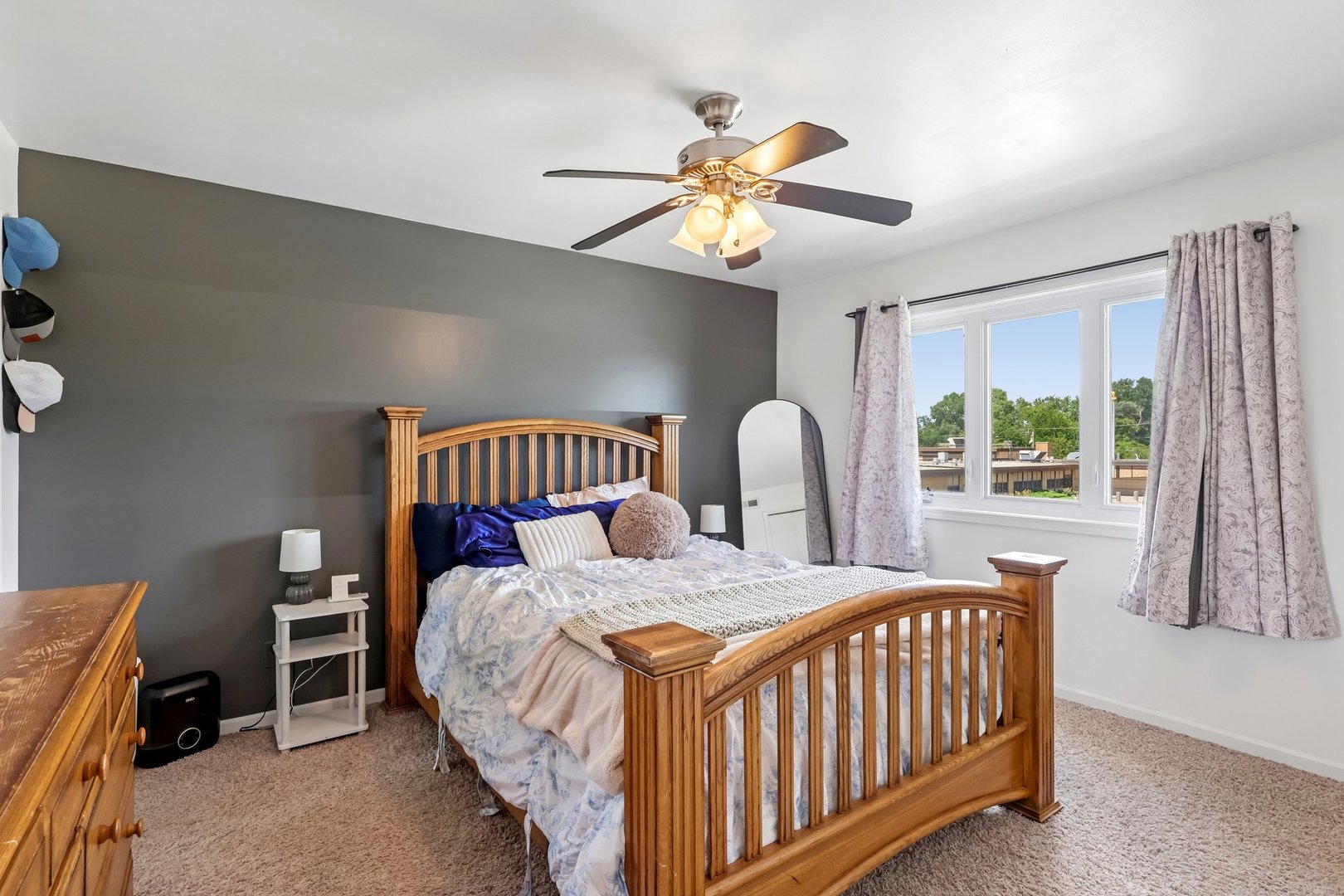 Bedroom with a wooden sleigh bed, dark gray accent wall, and large curtained window.