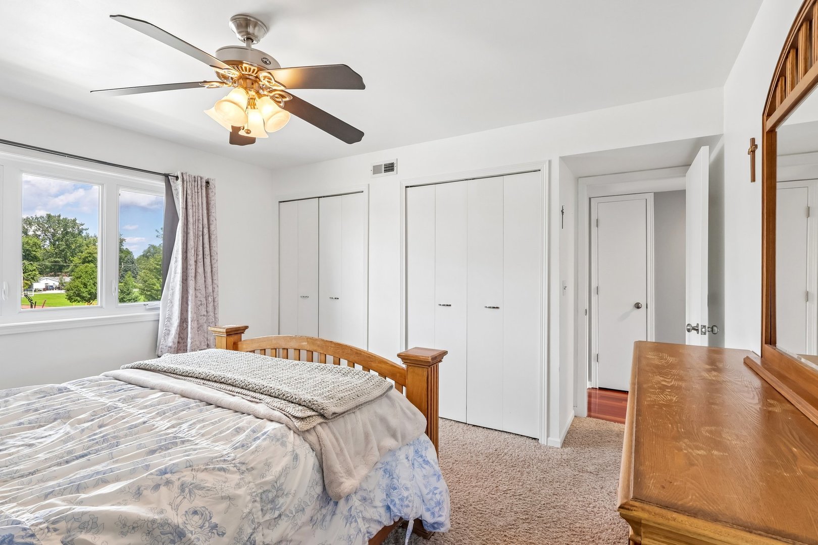 Bedroom with a wooden bed, ceiling fan, and windows overlooking trees.