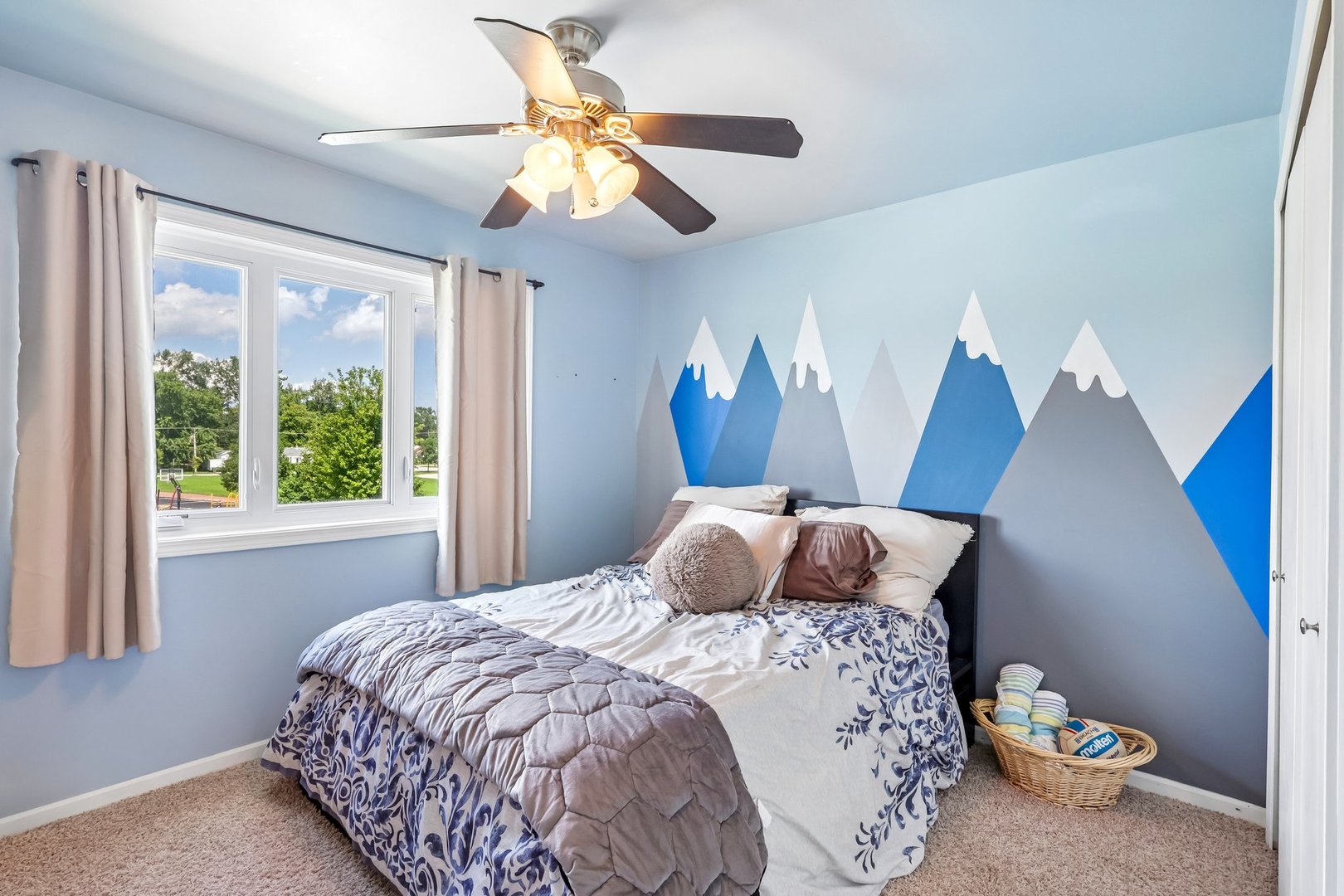 Bedroom with a blue mountain mural behind the bed and a ceiling fan overhead.