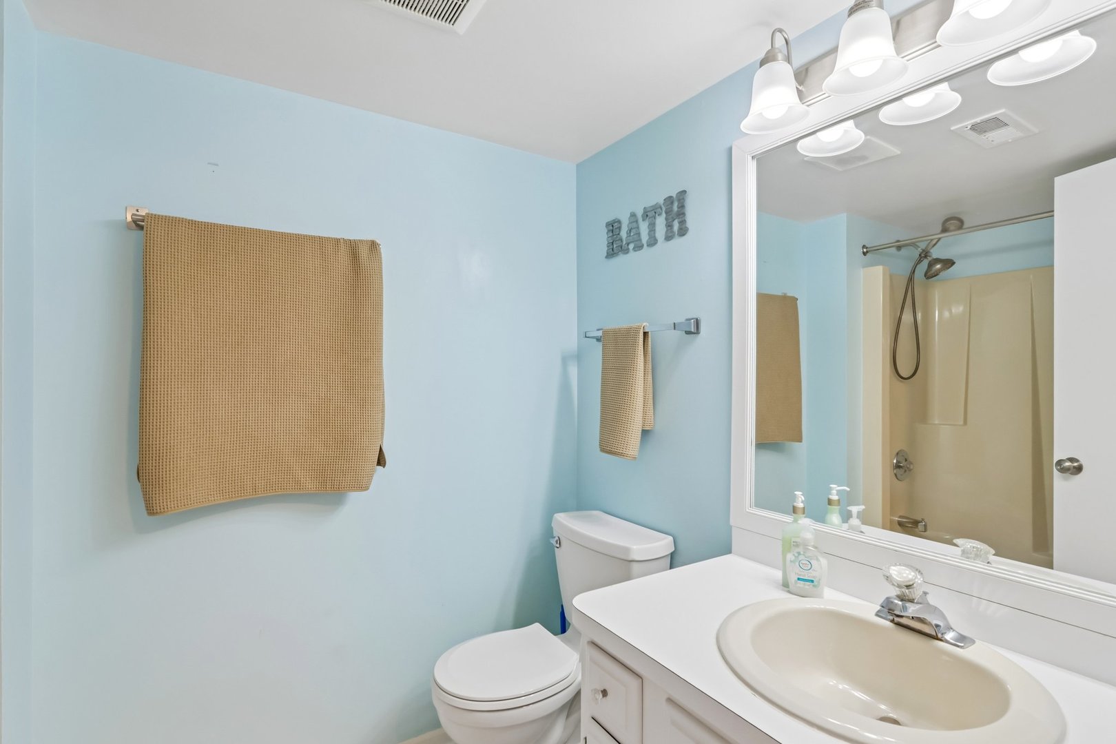 Bathroom with pale blue walls, white vanity and large mirror reflecting a beige shower.