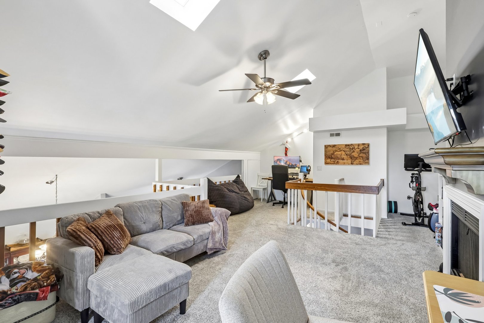 Furnished loft living area with a gray sectional, vaulted ceiling, and railing overlooking the lower level.