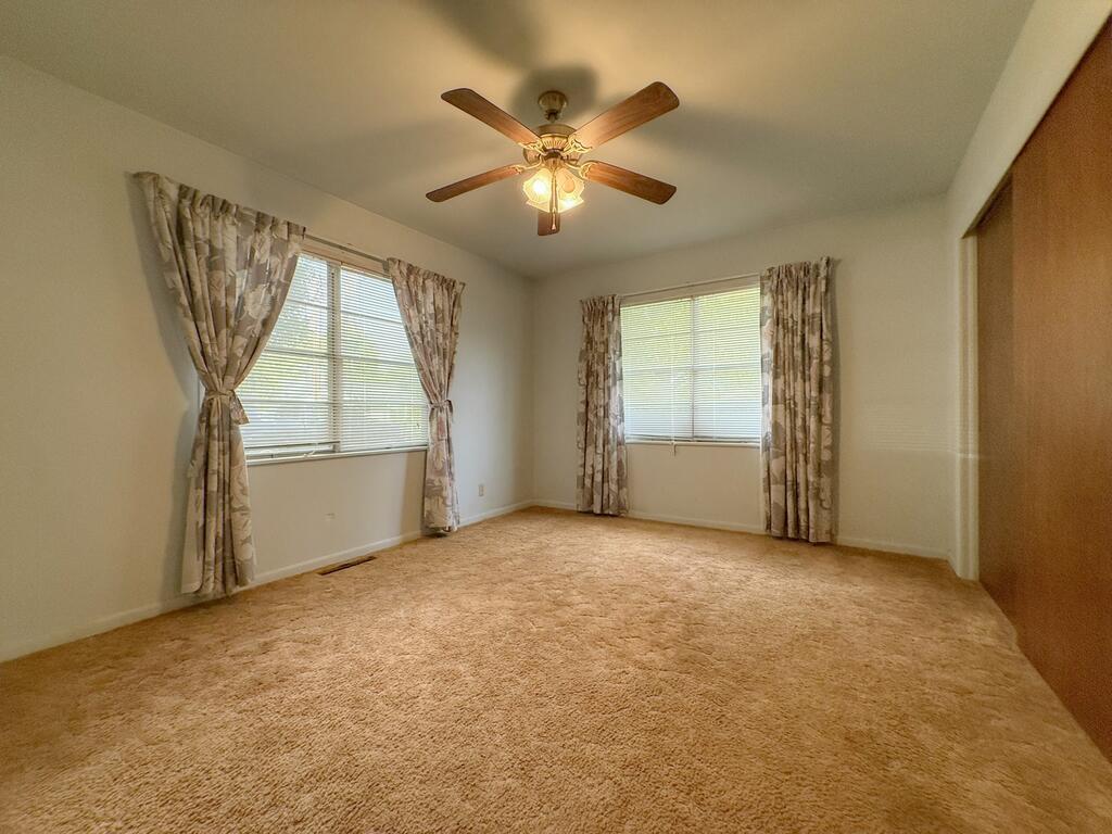 Empty carpeted bedroom with two curtained windows and a ceiling fan.