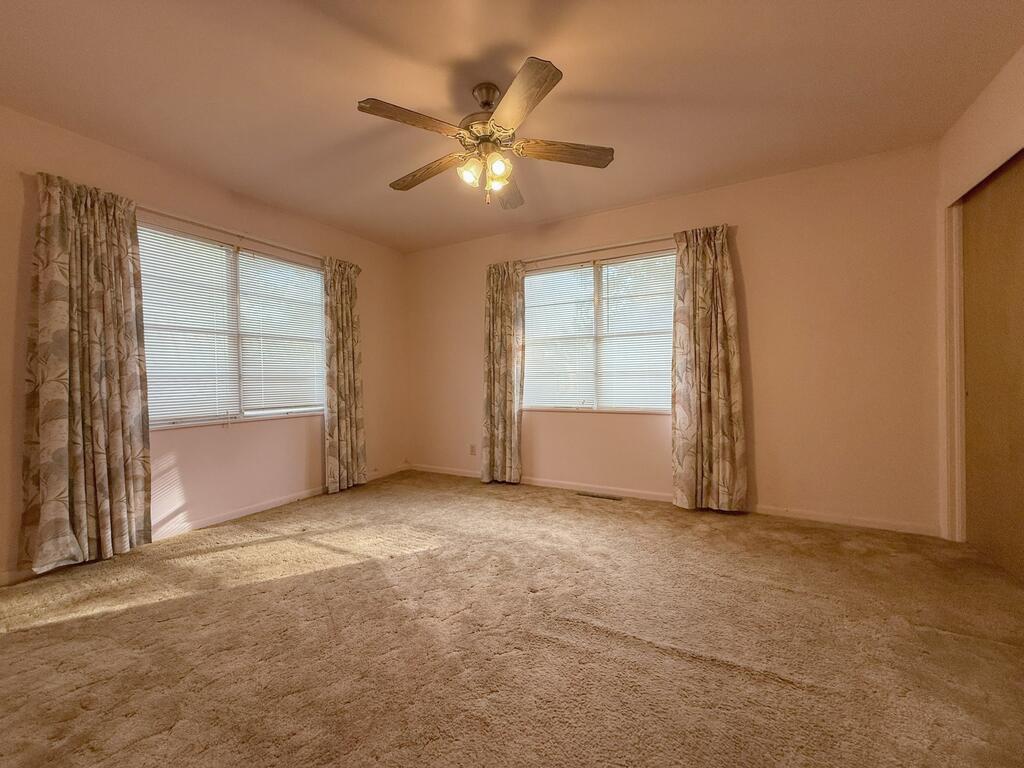 Empty carpeted bedroom with two curtained windows and a ceiling fan.