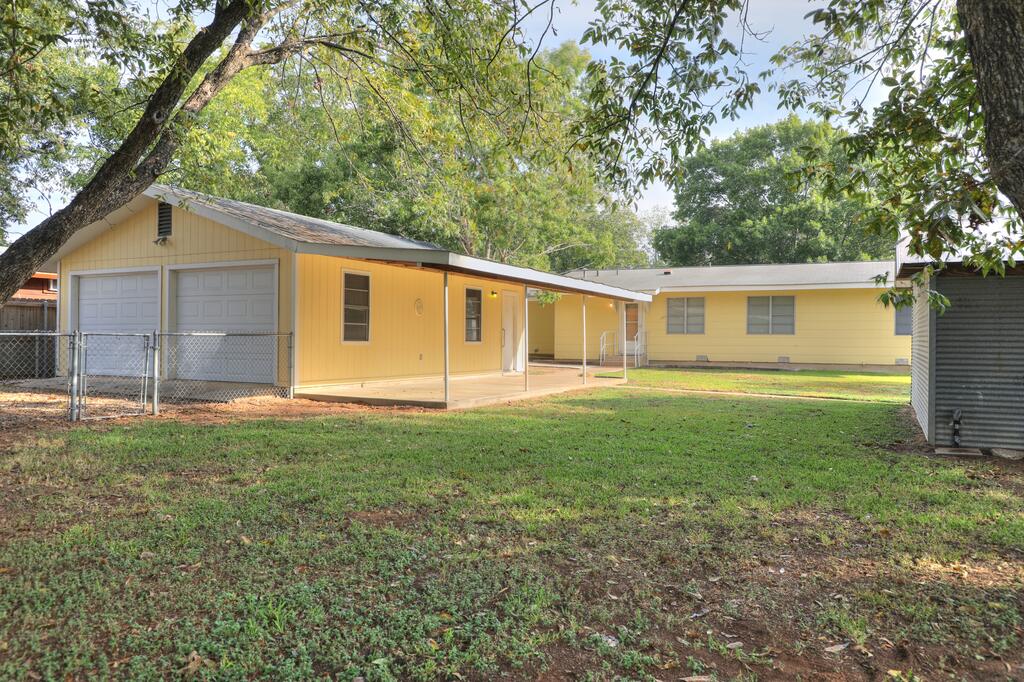 Yellow home and garage beside a broad grassy yard shaded by mature trees.