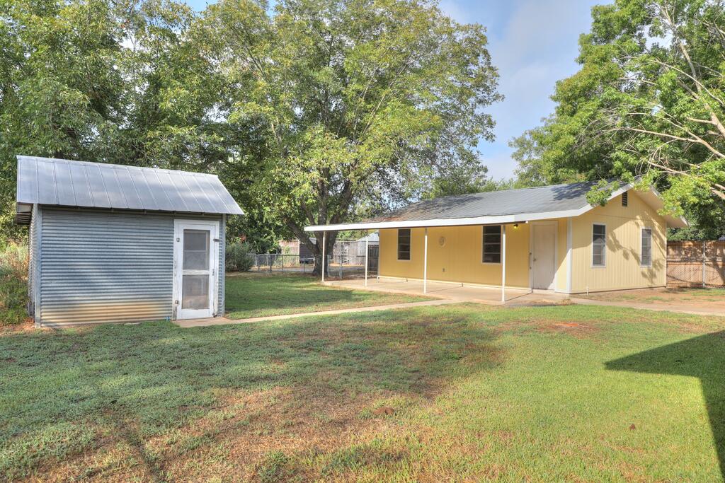 Yellow single-story house with a covered porch beside a small metal shed.