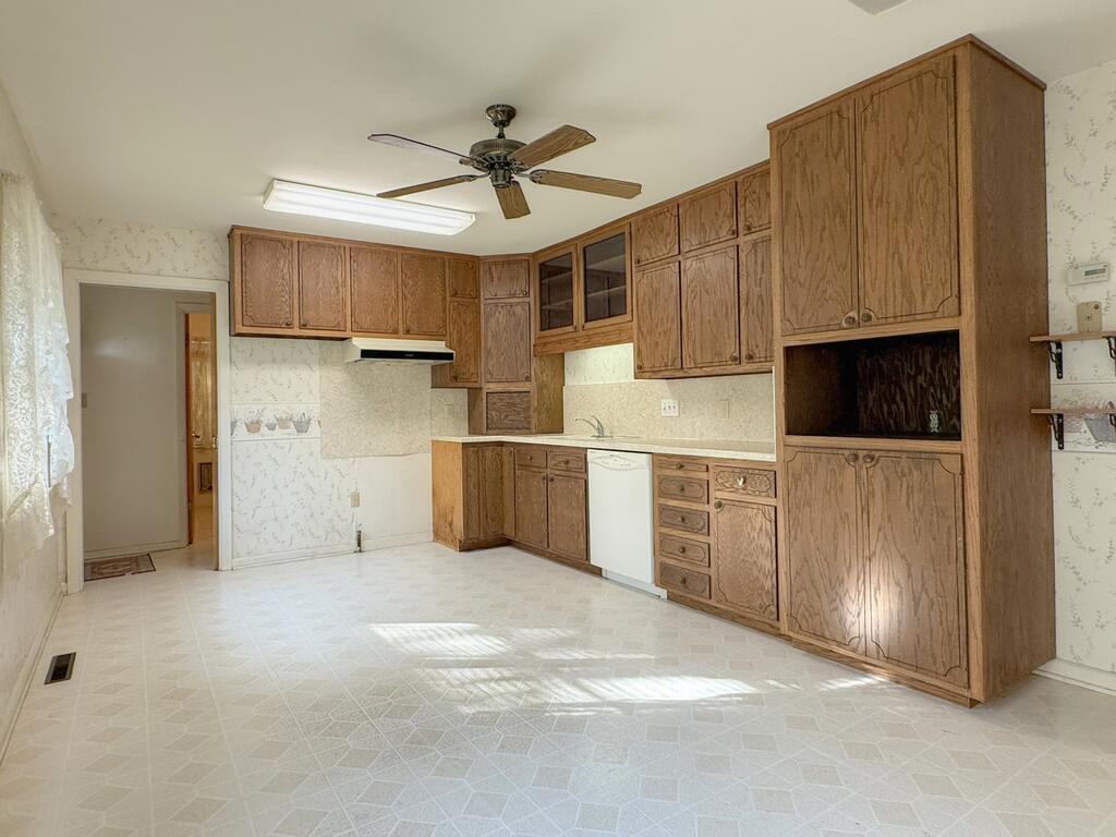 Empty kitchen with extensive oak cabinets, a white dishwasher, and patterned vinyl flooring.