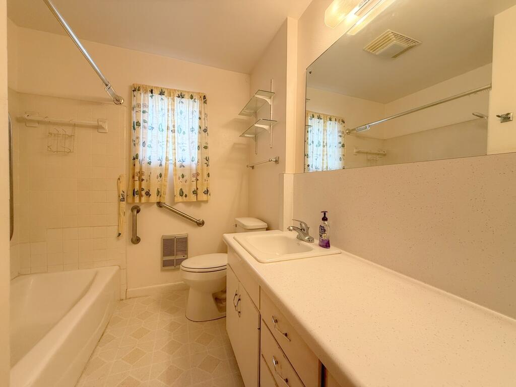 Bathroom with a bathtub, toilet, and long vanity beneath a large mirror.