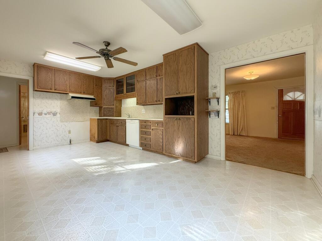 Empty kitchen with wood cabinets, ceiling fan, and doorway to an adjoining room.