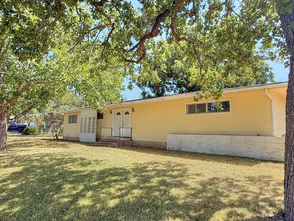 Pale yellow single-story home with double front doors beneath large trees and a shaded lawn.