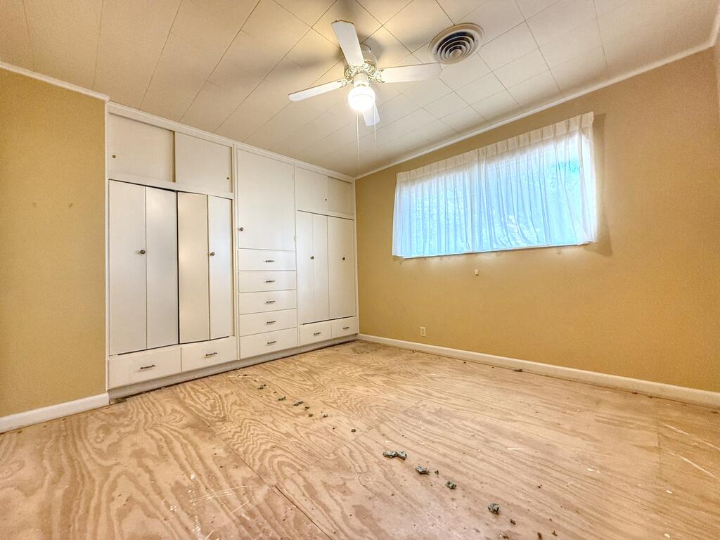 Vacant bedroom with built-in white cabinets, a ceiling fan, and exposed plywood flooring.