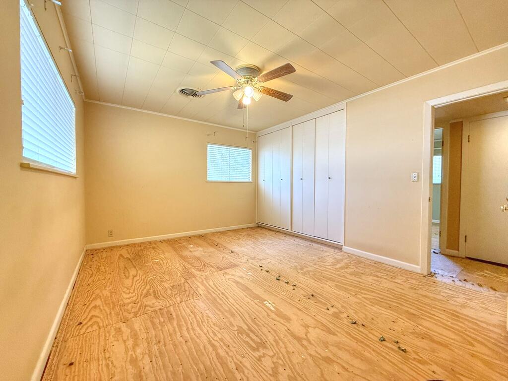 Empty bedroom with built-in closets, ceiling fan, and exposed plywood flooring.
