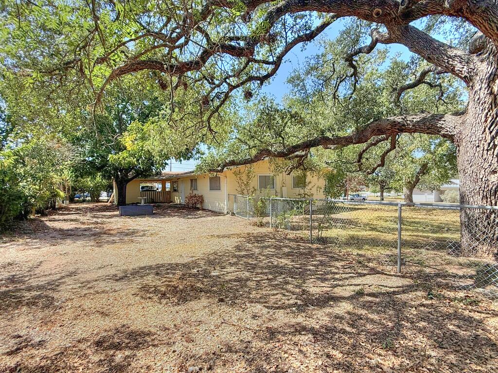 Single-story house behind a chain-link fence beneath a sprawling oak tree.