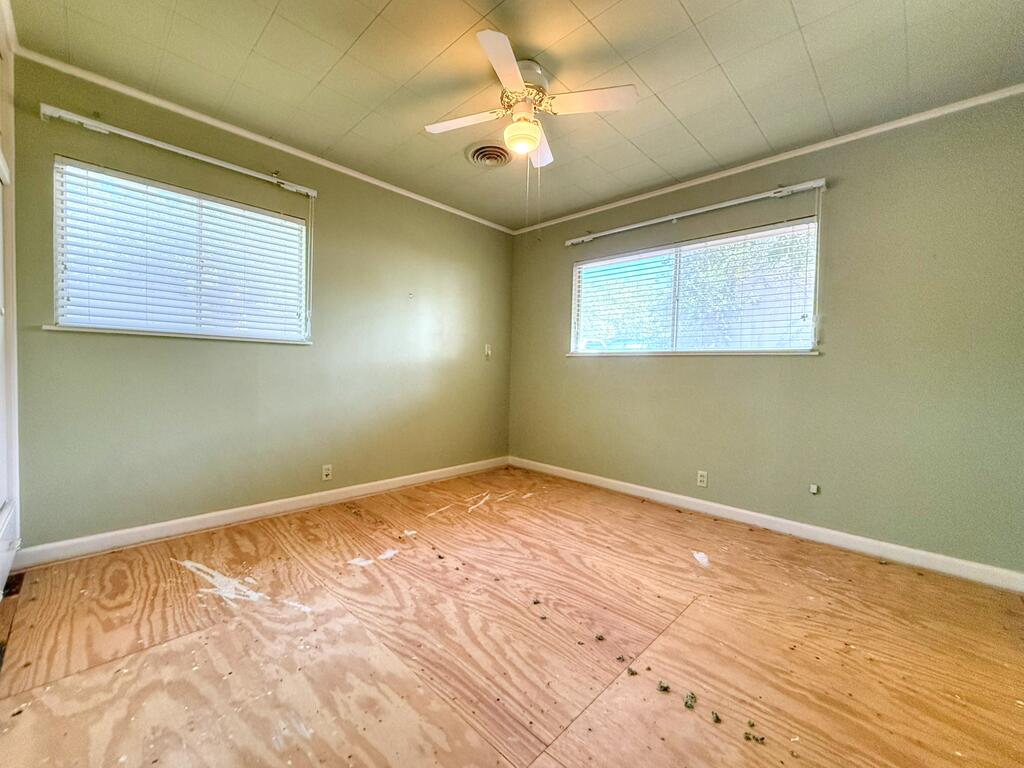 Empty room with two windows, a ceiling fan, and exposed plywood flooring.