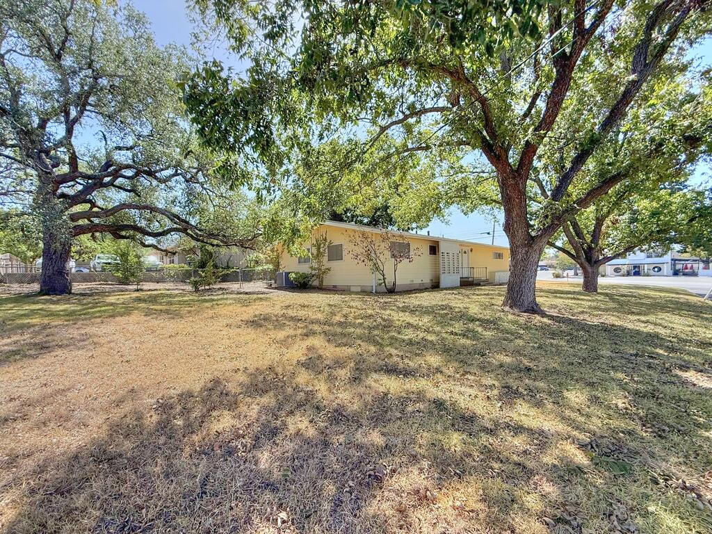 Single-story pale yellow building in a grassy yard beneath large mature trees.
