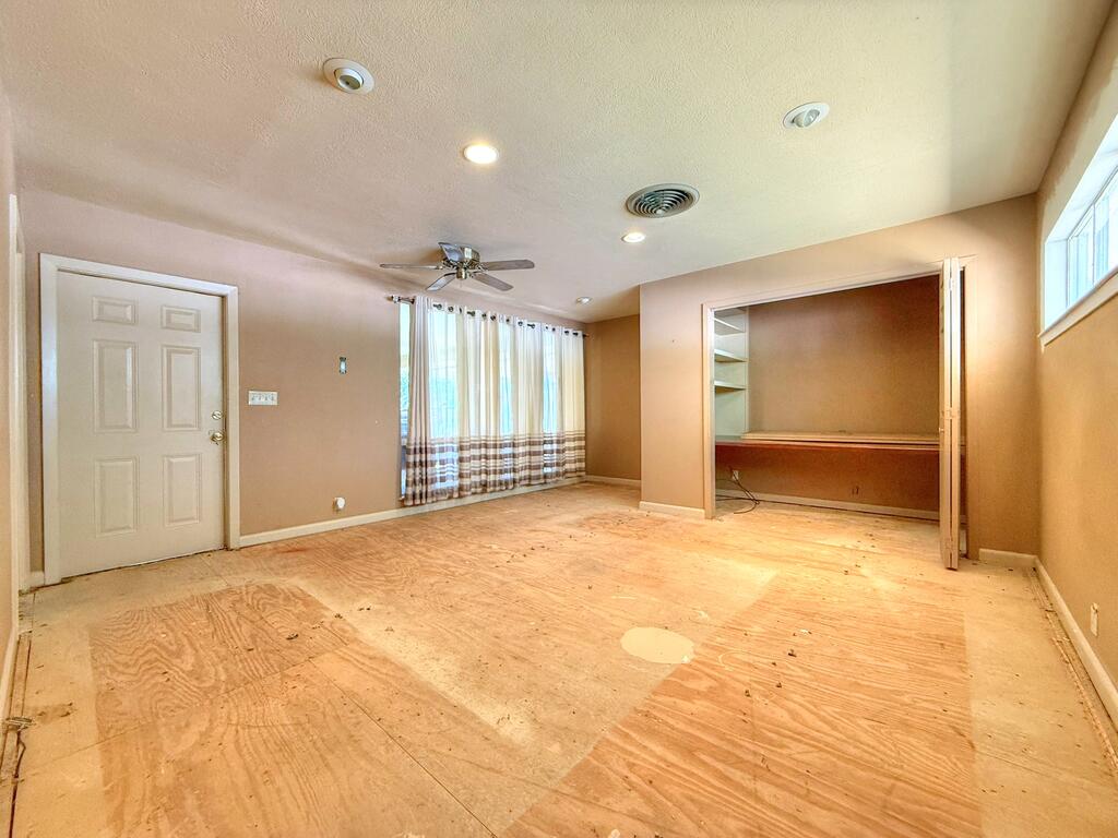 Empty room with plywood flooring, ceiling fan, curtained windows, and an open closet.
