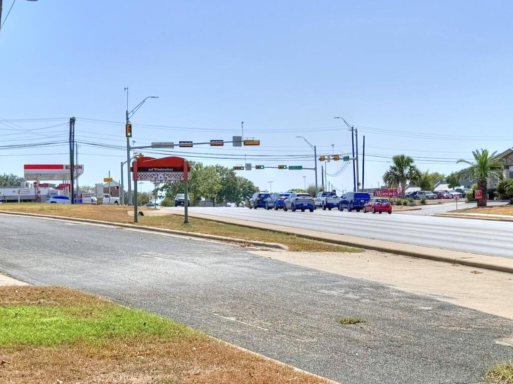 Wide intersection with traffic lights, passing vehicles, and roadside businesses.