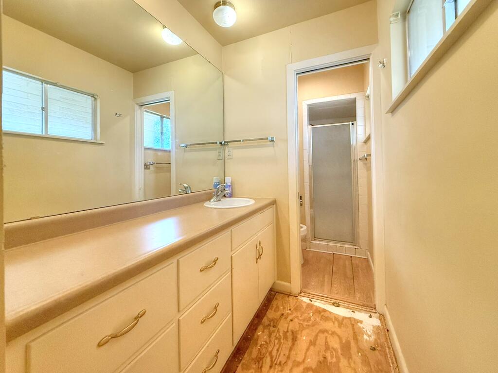 Bathroom with a long beige vanity, large mirror, and shower enclosure beyond the doorway.