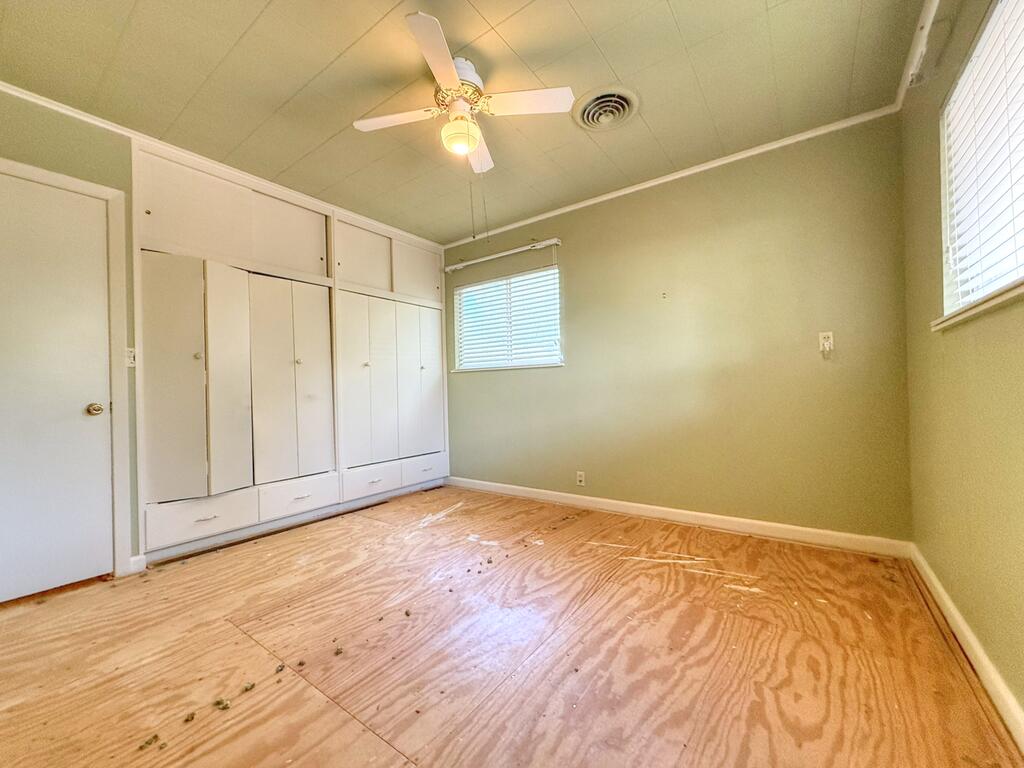 Vacant bedroom with built-in closets, plywood flooring, and a ceiling fan.