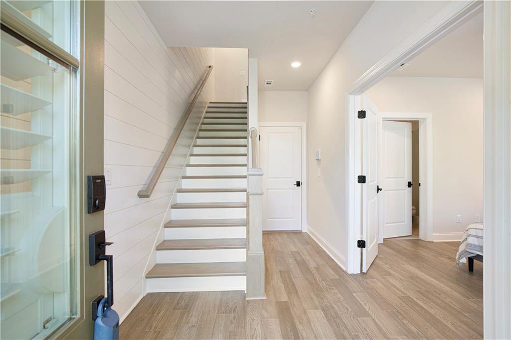 Entryway with a white staircase, shiplap wall, glass-panel door, and light wood flooring.