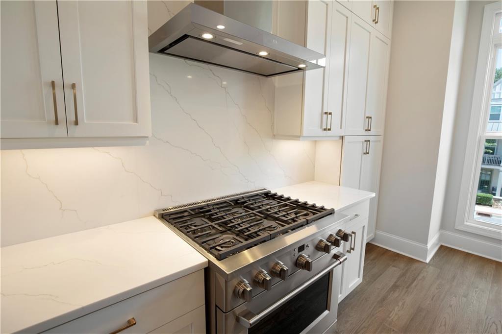 Kitchen with a stainless steel gas range, white cabinetry, and veined countertops.