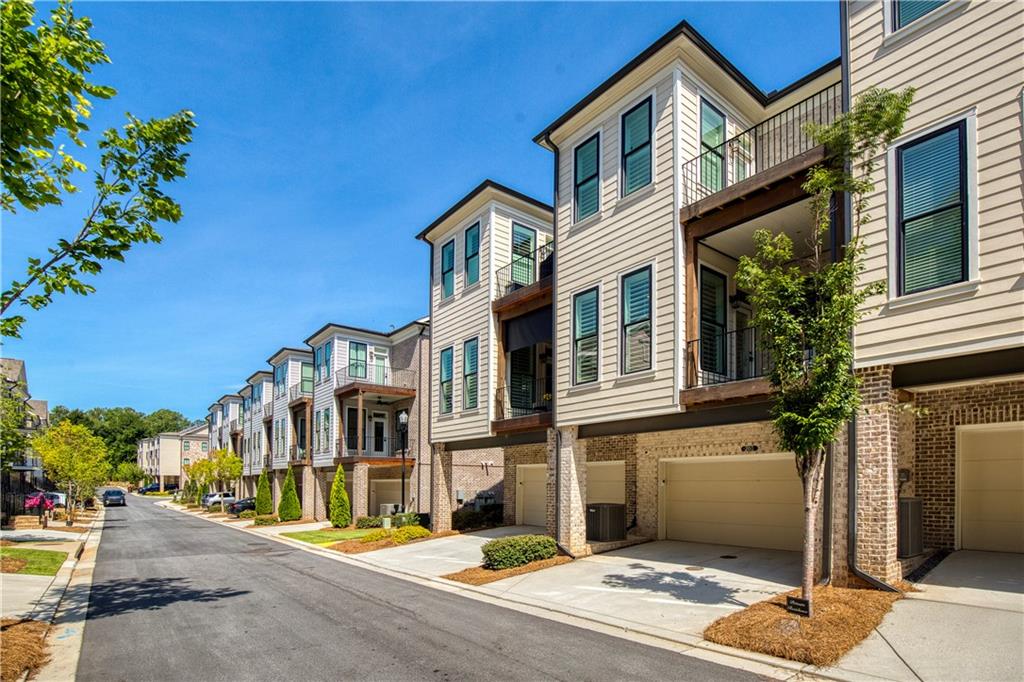 Attached townhomes with balconies and garage doors lining a sunny residential street.